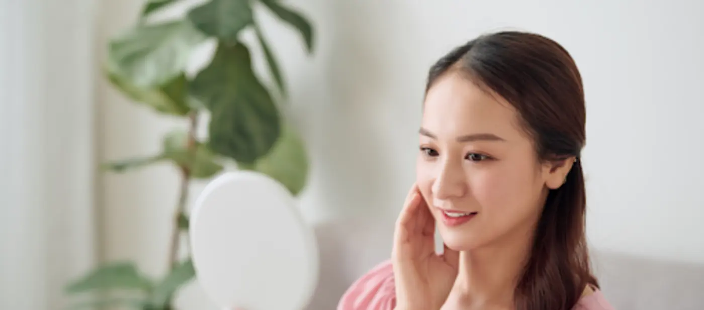 Wanita melihat cermin sambil memeriksa kulit wajahnya berkaitan dengan simptom kayap di muka atau kayap kulit.