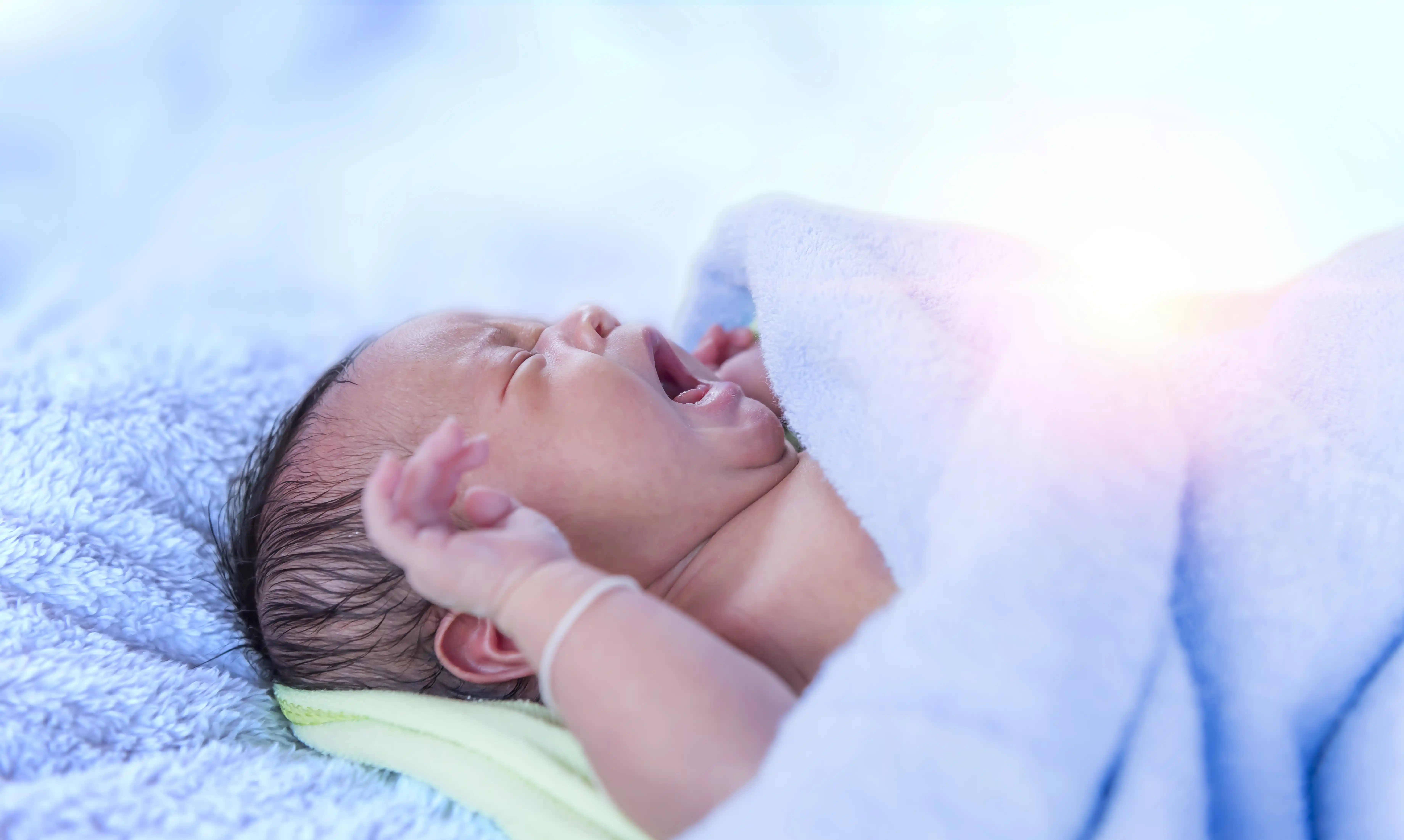 Crying newborn baby, possibly displaying signs of jaundice